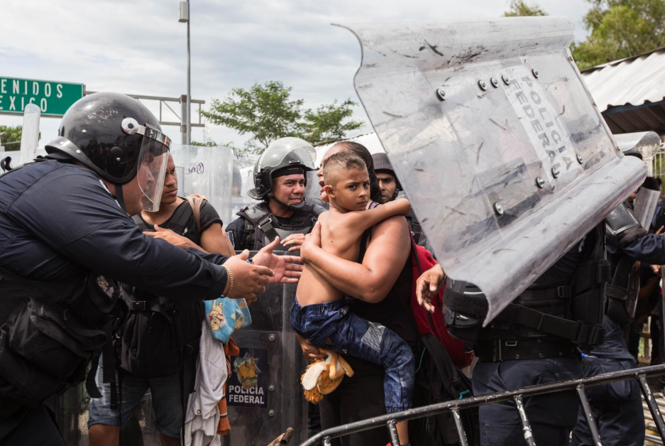 Viernes 19 de octubre. los migrantes forzaron el portón mexicano, pero no consiguieron sobrepasar al contingente de policías federales antimotines que los replegaron usando gas lacrimógeno. En la fotografía, policías mexicanos intentan calmar a un niño que viajaba con su madre (Fuente: Fred Ramos, El Faro).