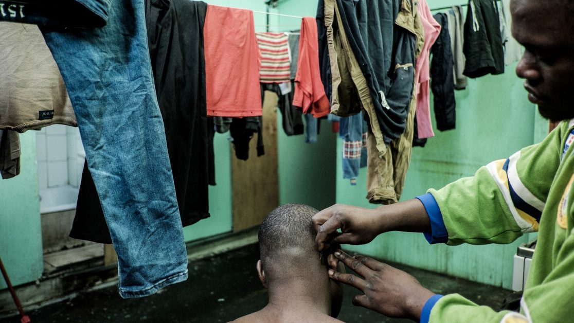 Un haitiano le corta el pelo a uno de sus coterráneos en el pasillo –que también hace de cocina- del segundo piso. Foto: Jorge Vargas | Migrar Photo