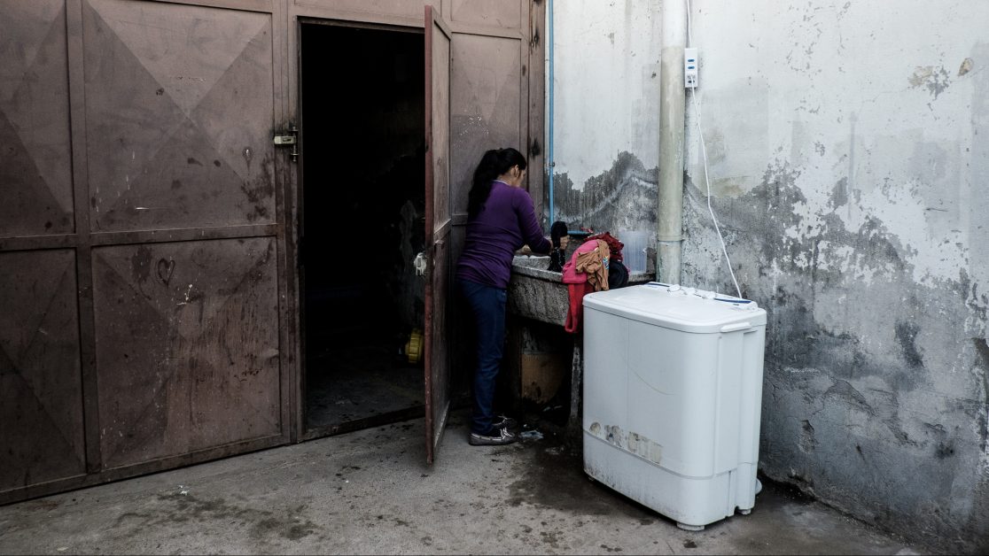 Una mujer, de origen peruano, lava su ropa en el único lugar con luz natural del galpón. Foto: Jorge Vargas | Migrar Photo